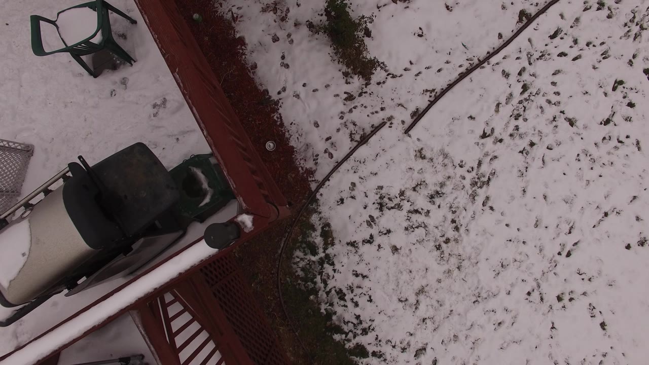 Overhead snowy backyard with red fence and patio furniture.