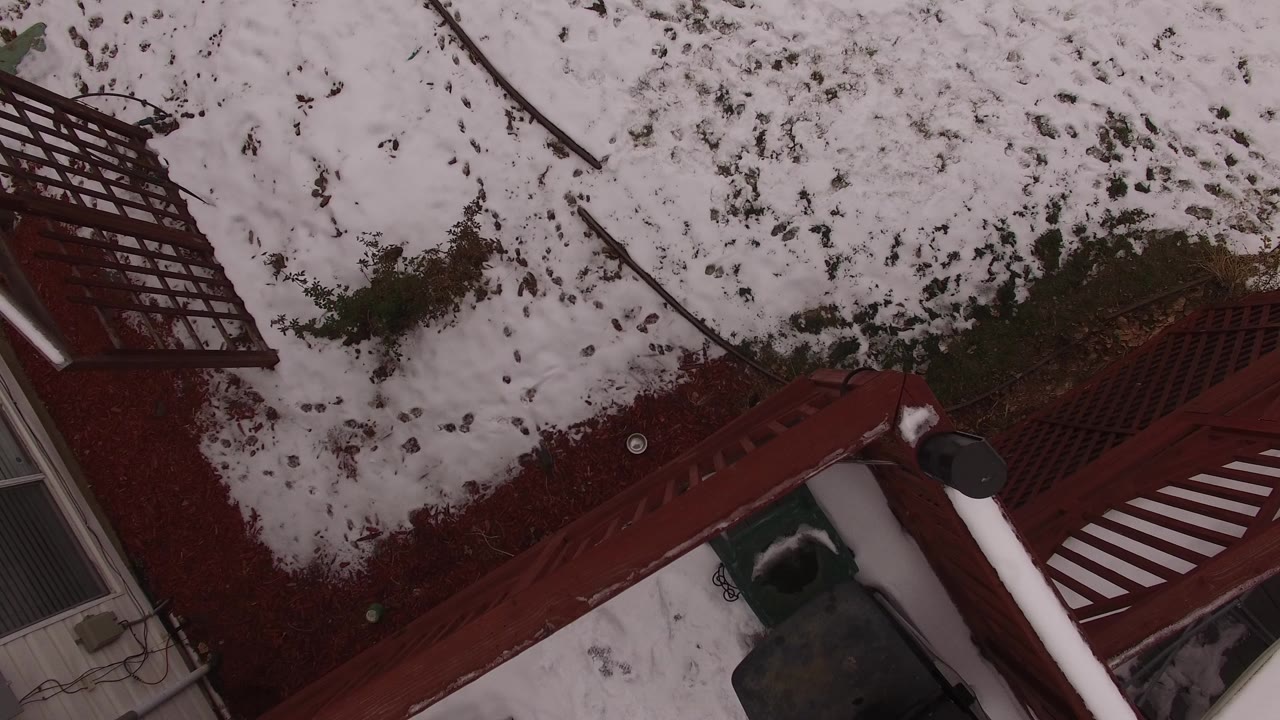 Top-down Jefferson, Colorado winter view of snow-covered ground beside red deck railings and a house edge, with no visible people.