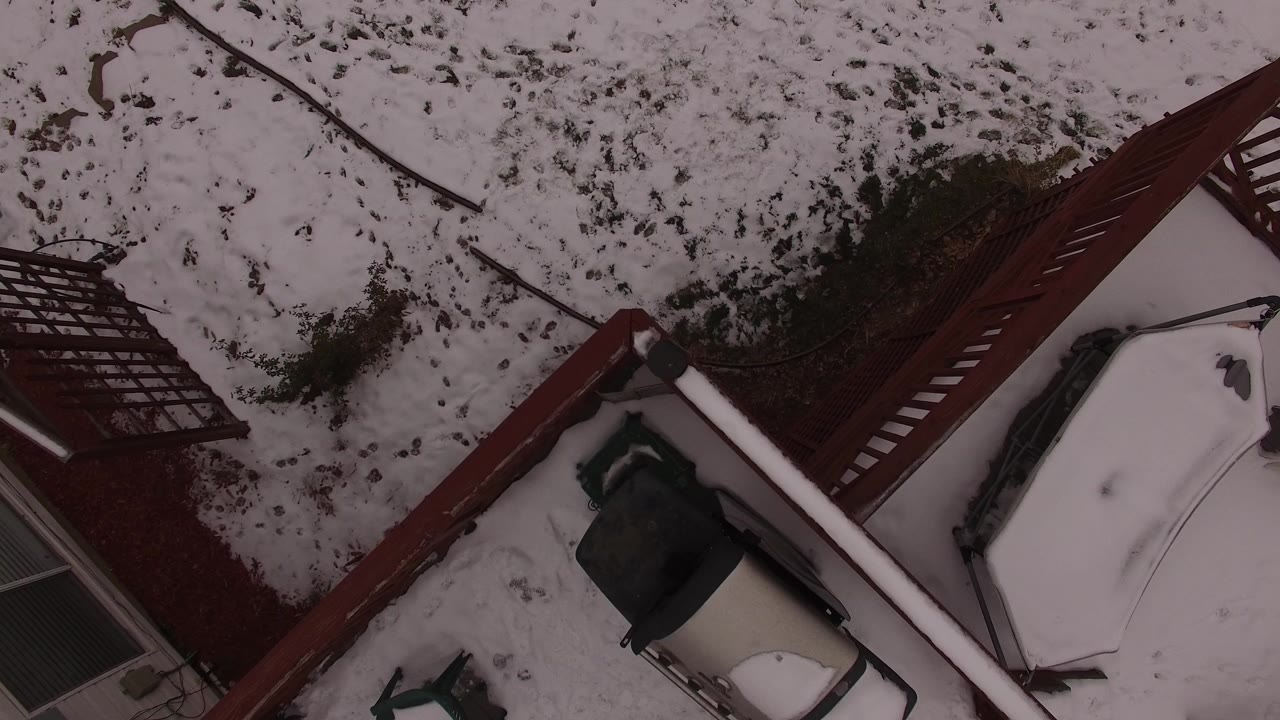 Overhead view of snow on a patio, deck, yard, and house exterior.