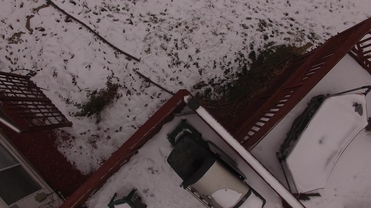Second frame in Jefferson County, Colorado holds on the snow-dusted yard, diagonal red deck structure, patio furniture or covered object, and house edge with no visible people.