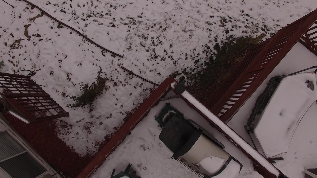 Overhead view of a snow-covered house roof and red deck beside a snowy yard.