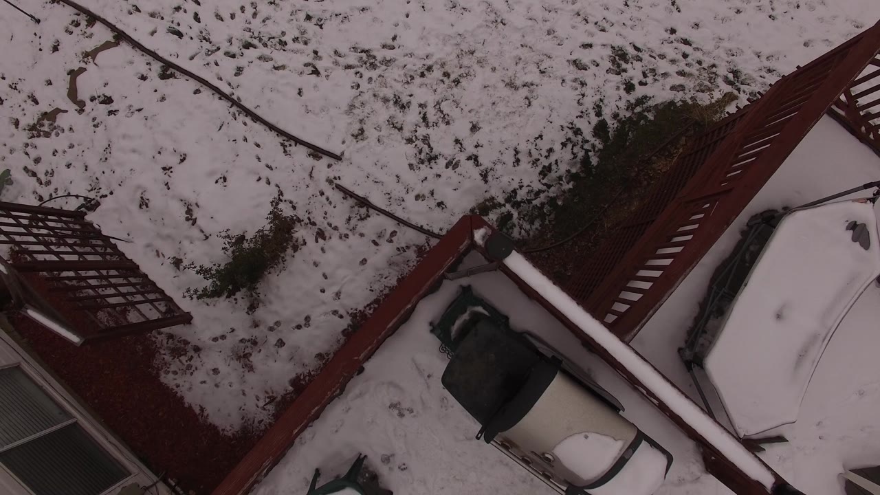 Overhead Jefferson, Colorado view with the red deck cutting diagonally across the frame, snow on the roof and yard, patio items near the house, and no visible people.