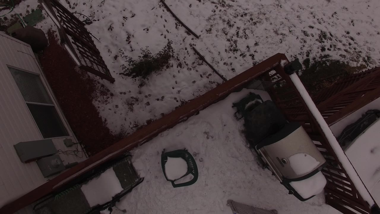 Overhead view of a snowy backyard with a brown red fence and house edge.