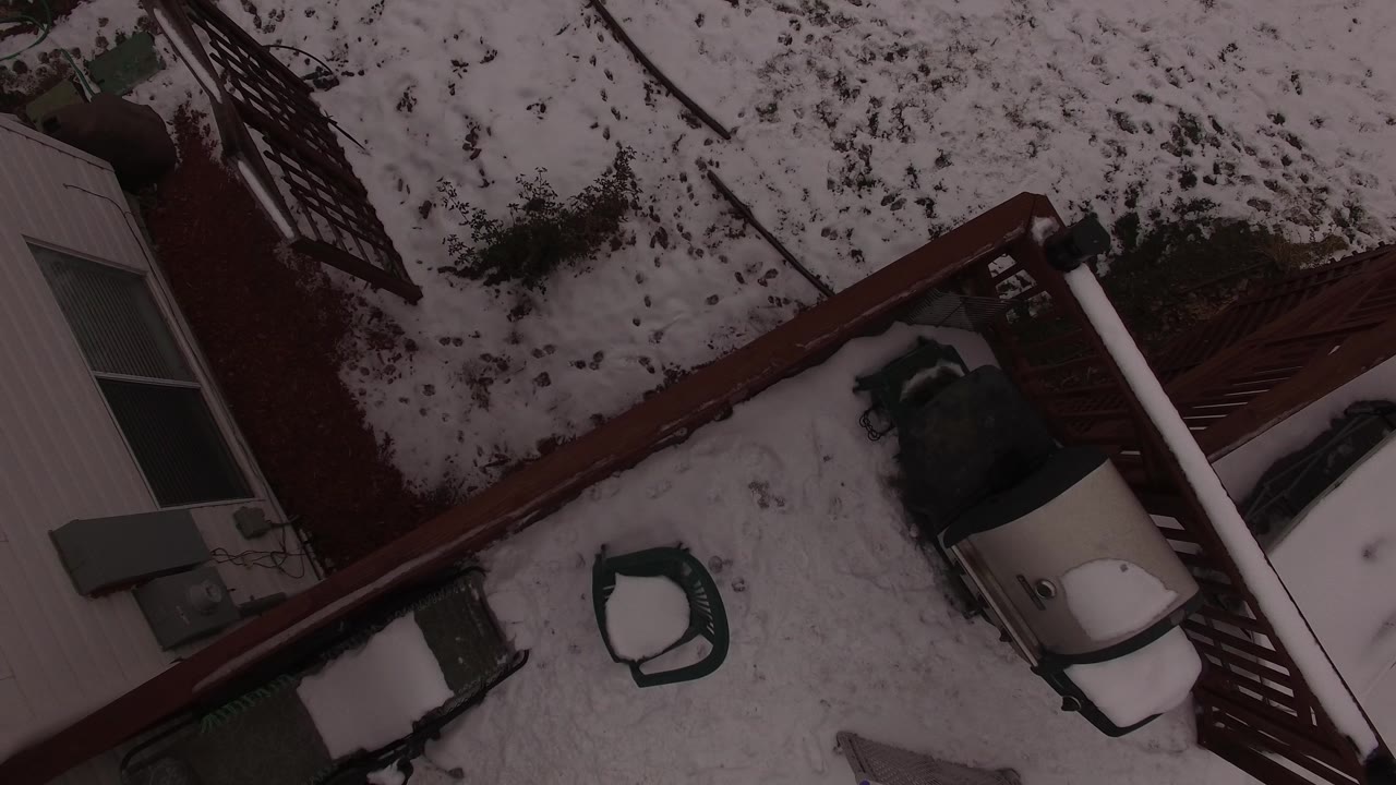 Overhead Jefferson County, Colorado view with the brown red fence crossing the snowy yard, a patio chair shape near center, house siding at left, and no visible people.
