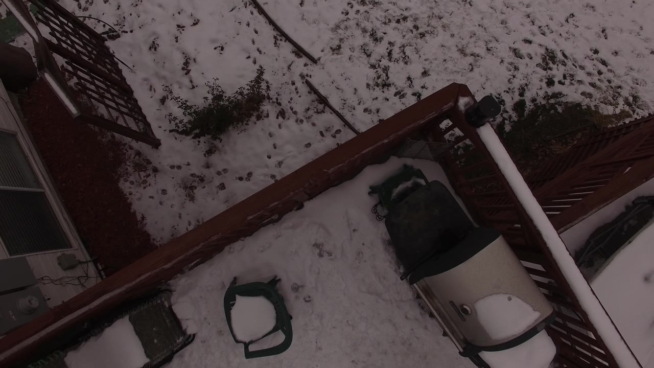 A Jefferson, Colorado backyard remains framed from above, with the red fence running diagonally beside snow, a dark chair, and cropped house exterior details, no visible people.