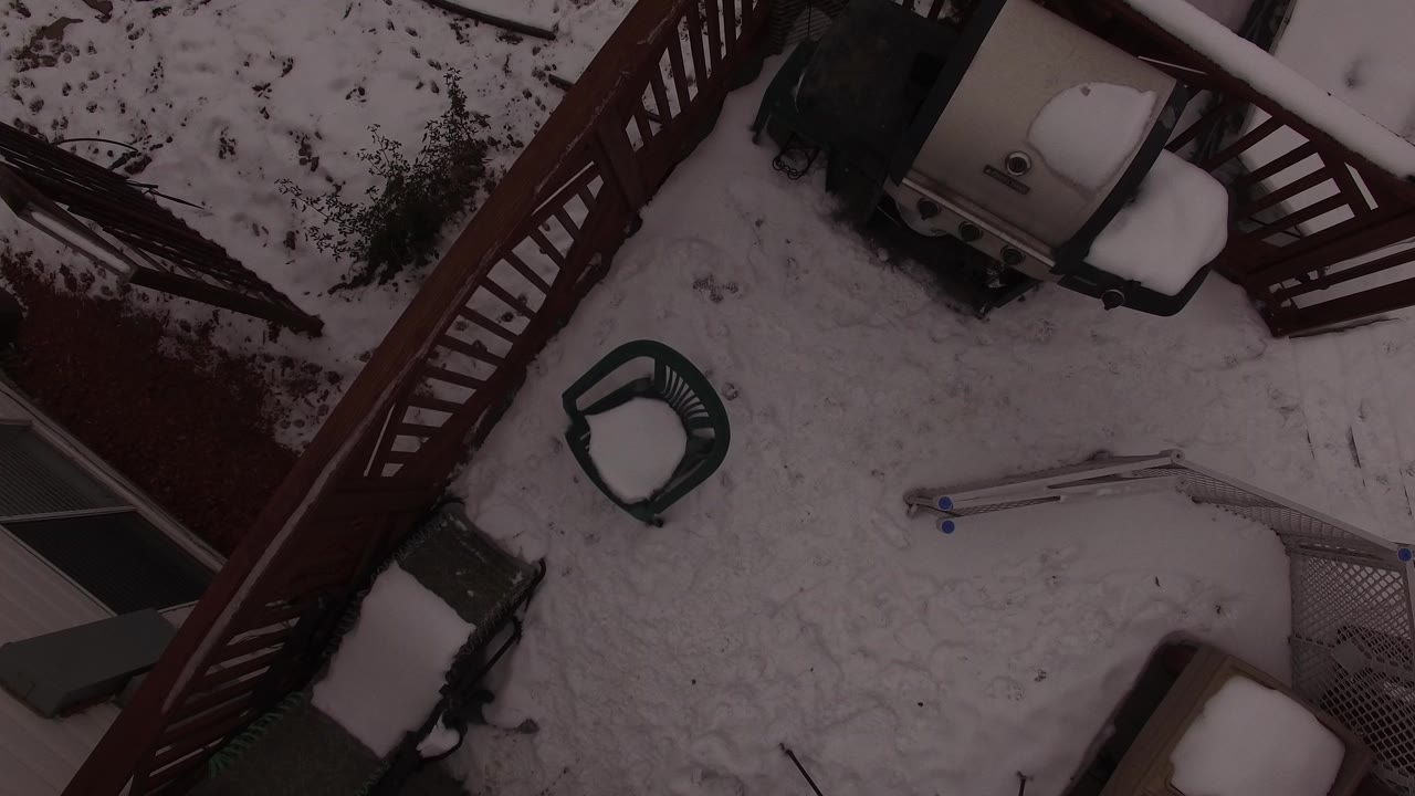 Snow-covered deck viewed from above with patio chairs and railings.