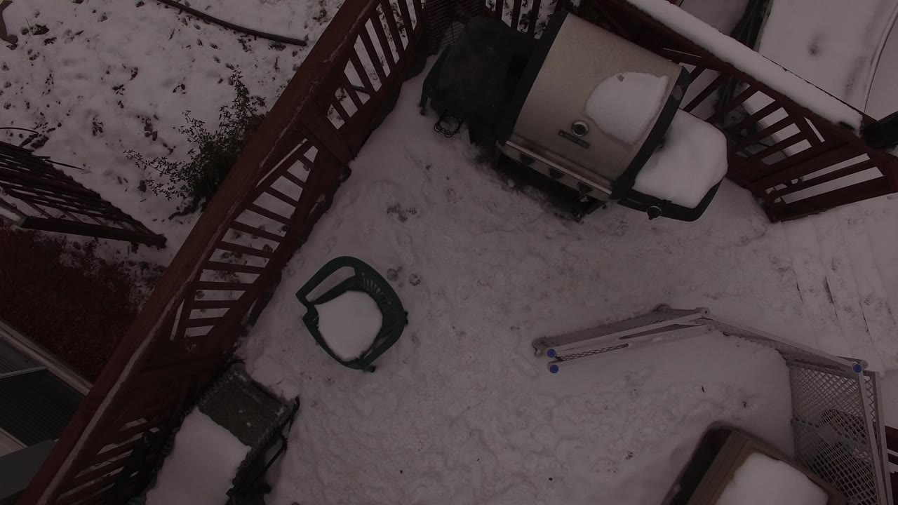 Top-down snowy deck with railing, covered grill, chairs, and ladder.