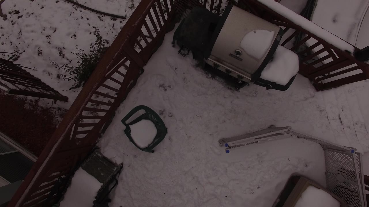 Overhead frame from Jefferson County, Colorado, with diagonal wooden deck railings, a covered barbecue grill, a snow-filled chair seat, a ladder, and no visible people.