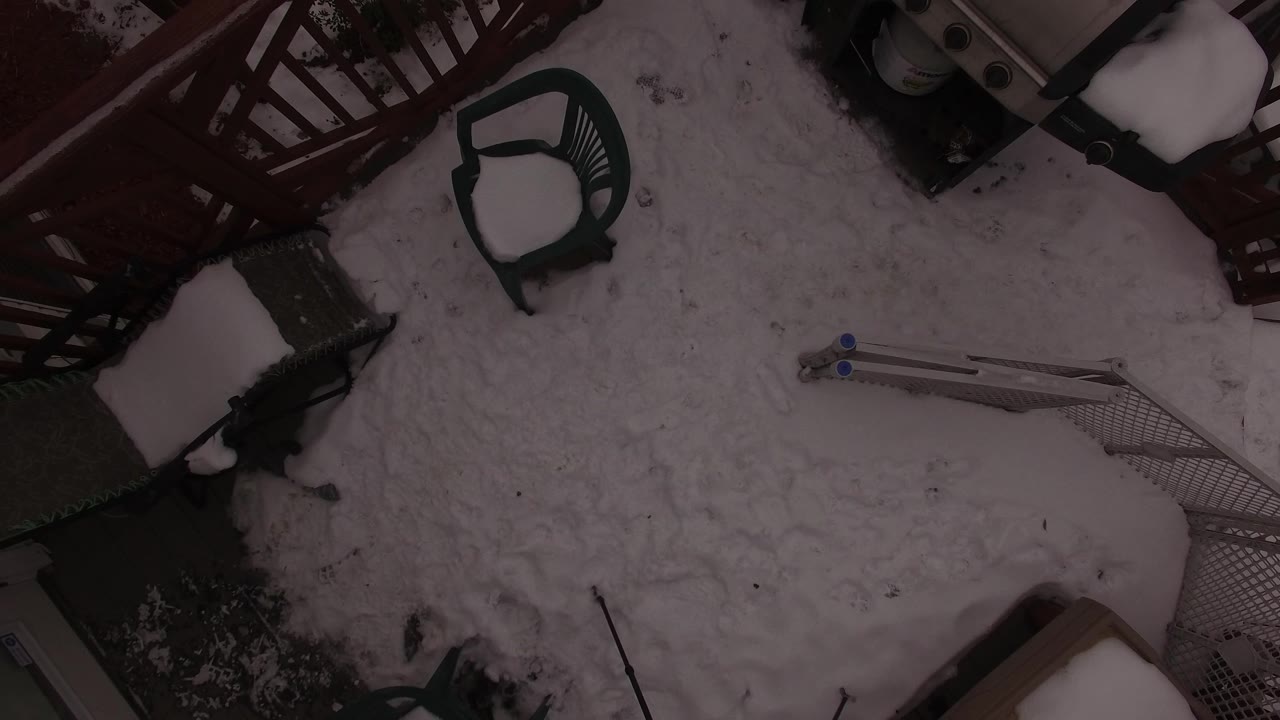 Aerial frame over the Jefferson County terrace showing compacted snow, a green chair near the red railing, a folded metal frame, and no visible people.