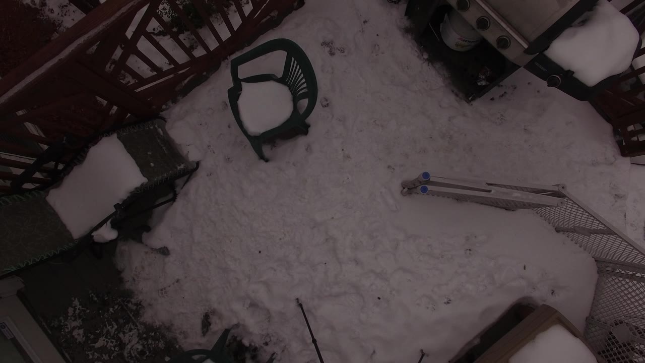 Top-down winter patio with red railing, chair, and snow-covered equipment.