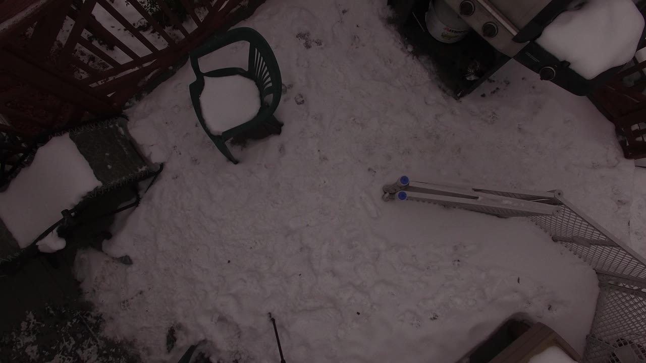 Snow-covered backyard seen from above with patio chair and fencing.