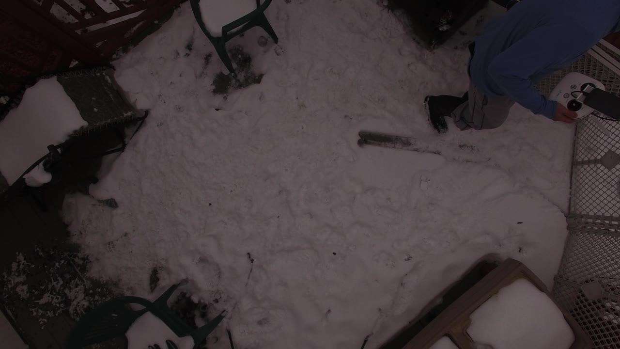 High overhead view in Jefferson County, Colorado showing a snow-covered residential yard, fence sections, patio chairs, and a dark dog-like shape near the left side, with no clearly visible face.