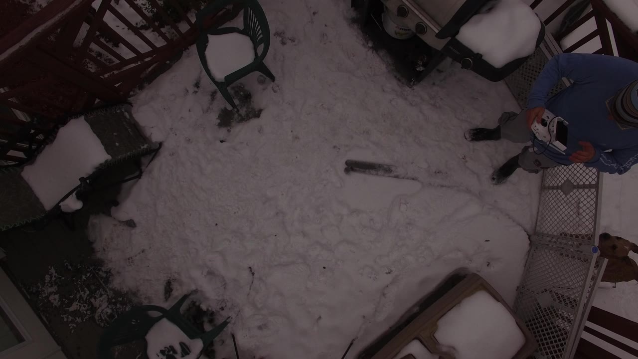Overhead view of a snowy deck with patio furniture and a partially visible person.
