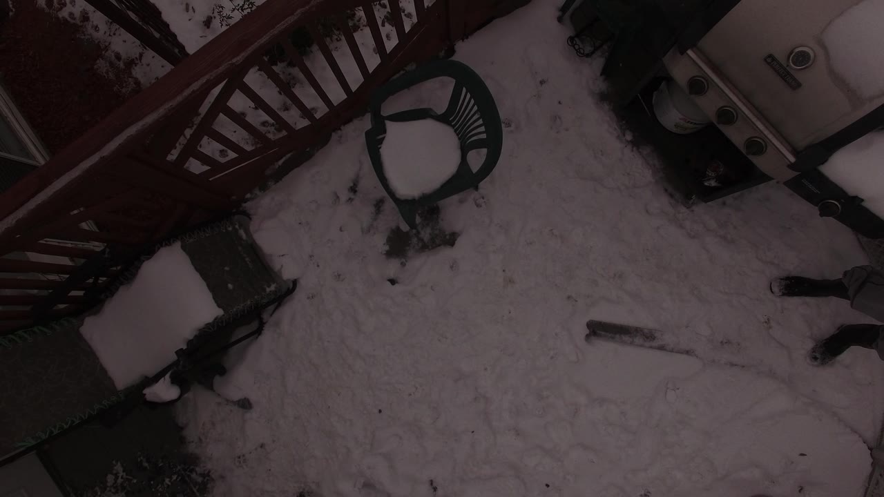Top-down view of a snowy patio with chairs, railing, and a grill.
