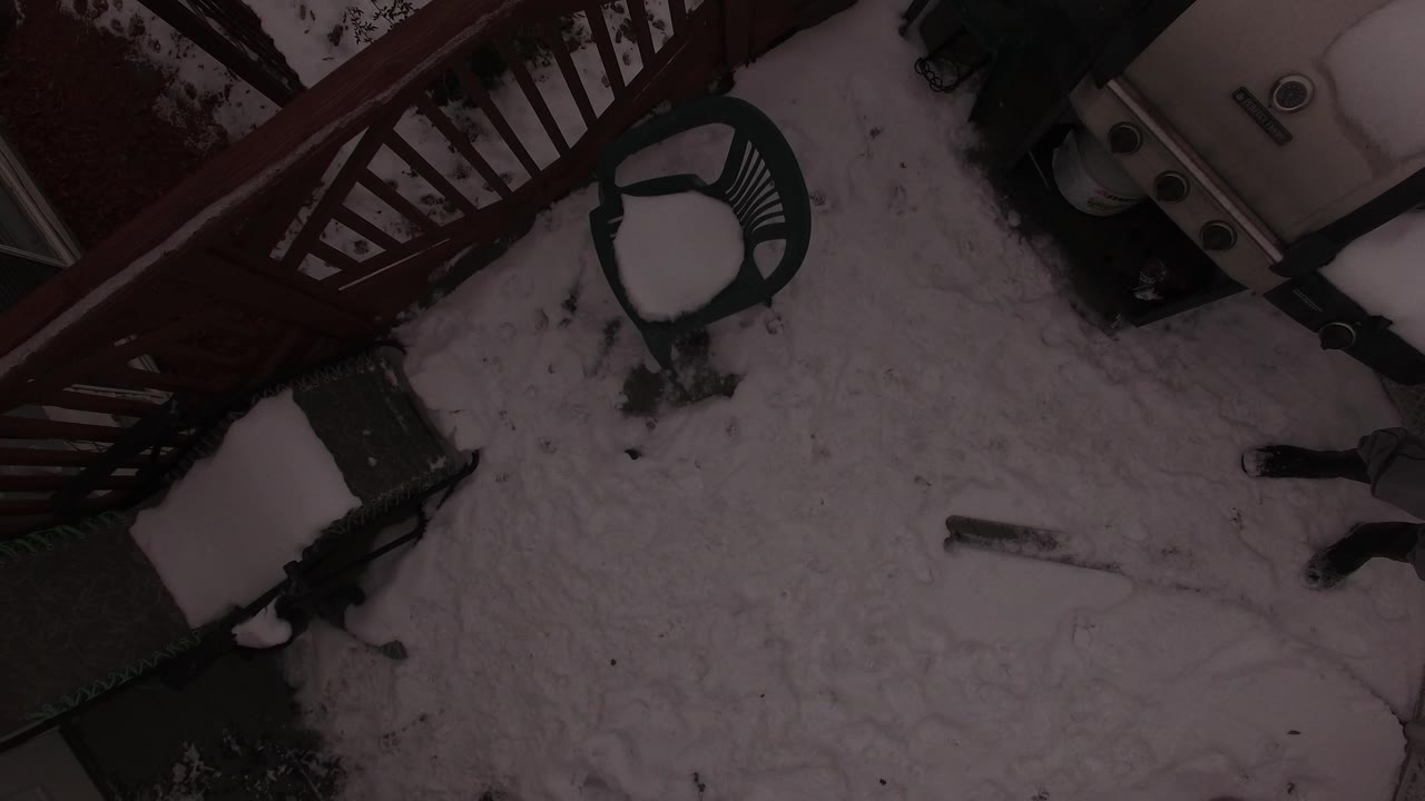Second overhead frame in Jefferson, Colorado with a plastic chair, snow-covered grill, red railing, and uneven snow across the patio, with no visible people.