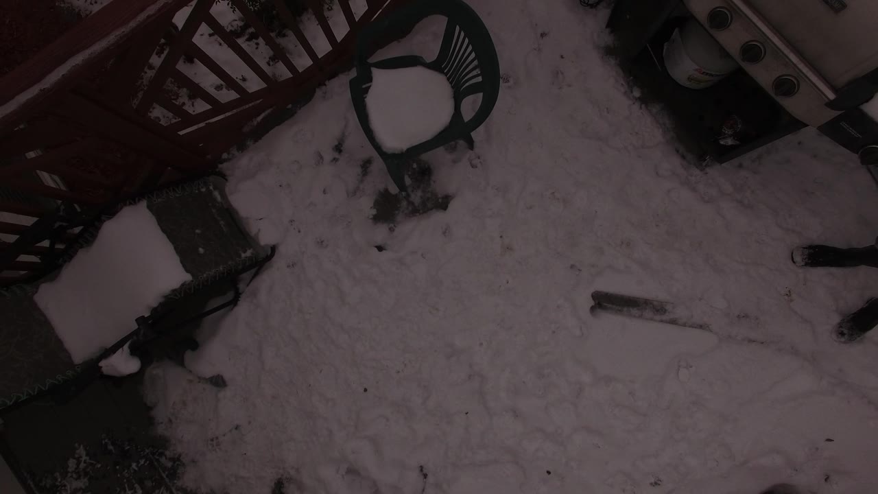 A dark overhead frame shows a snow-covered yard or patio area in Jefferson County, Colorado with deck railing, outdoor seating, and no visible people.