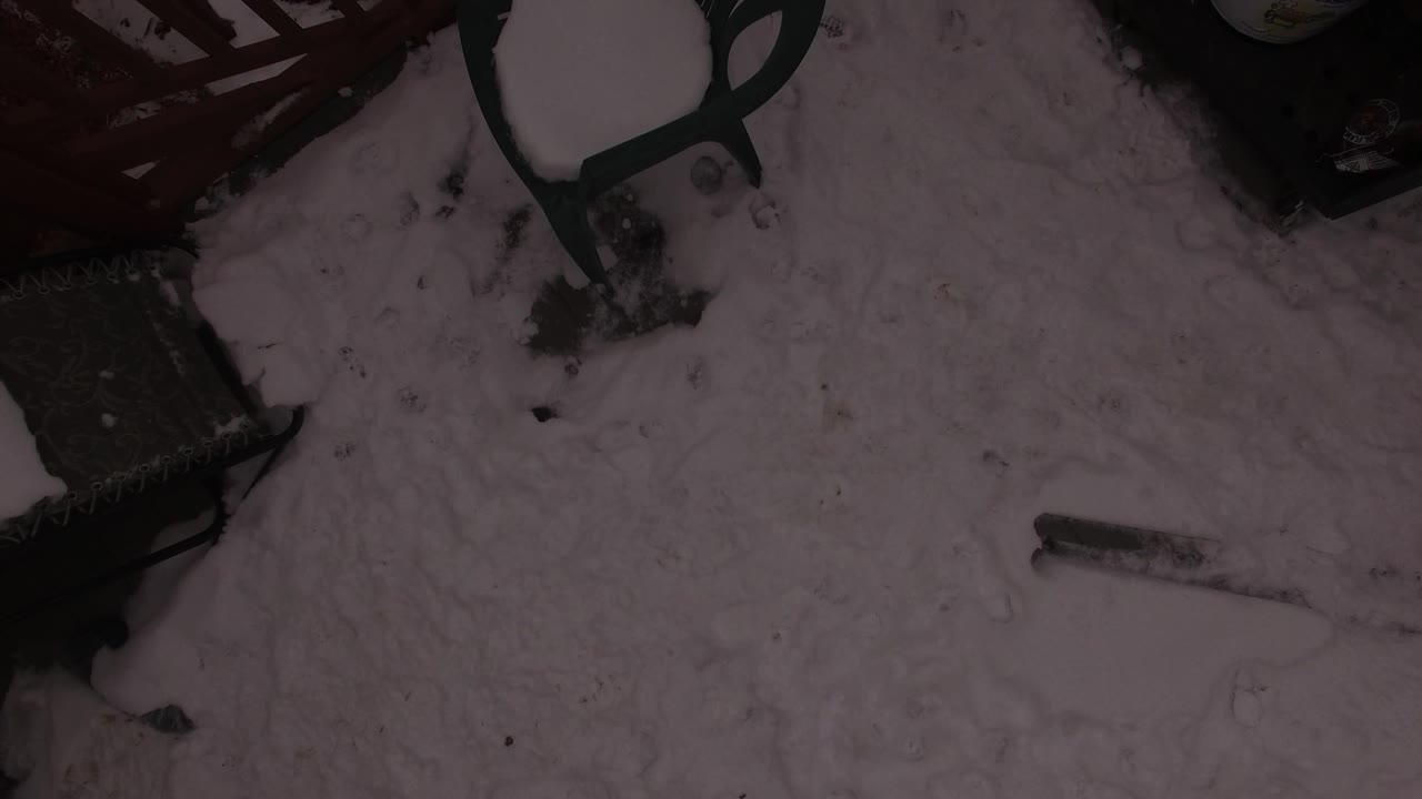 Angled snowy deck area with chairs and dark patio objects.