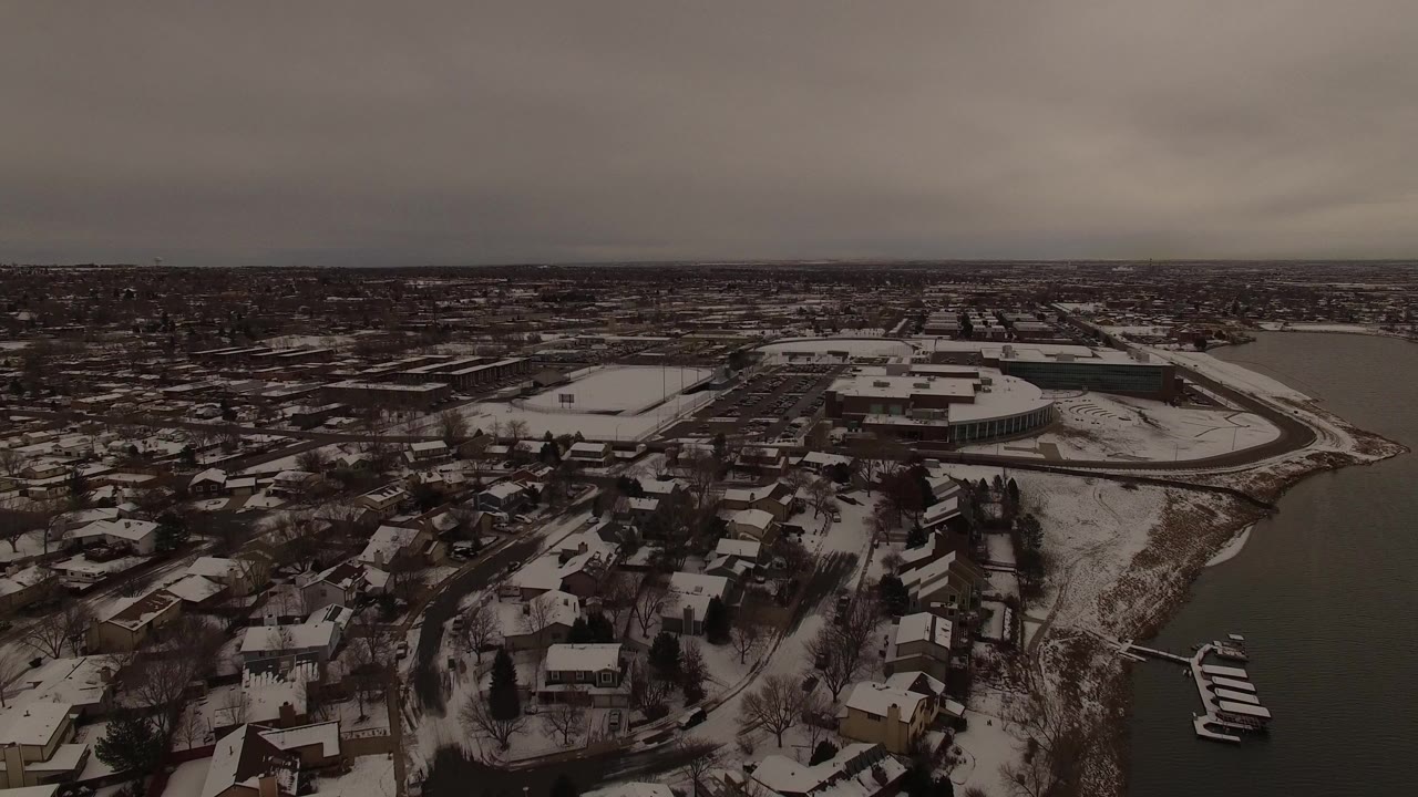 Aerial view over Jefferson County, Colorado homes with snowy roofs, a waterway on the right, docks near the lower right edge, and no visible people.