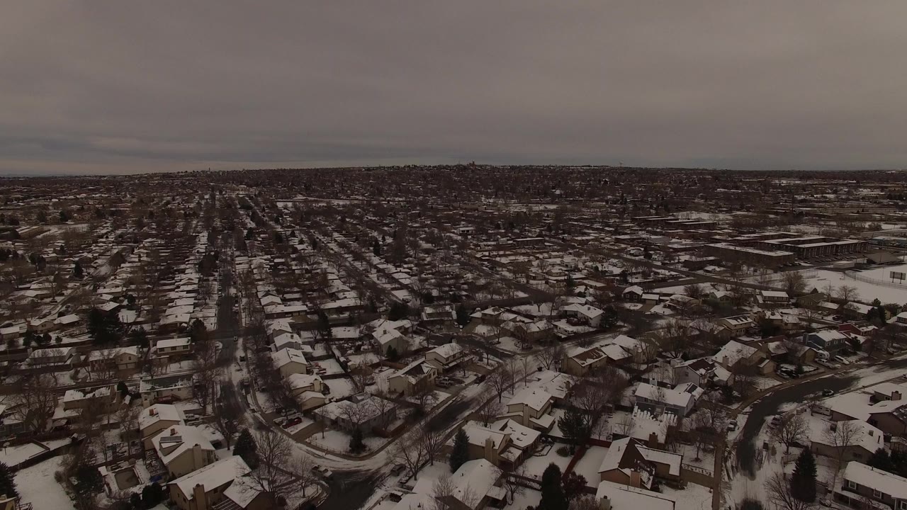Aerial view in Jefferson County, Colorado centered on a long residential street lined by snow-covered houses, bare trees, and no visible people.