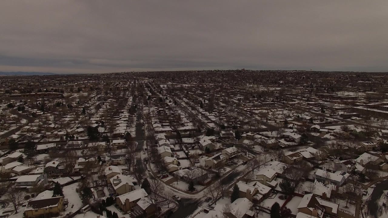 High view across snow-dusted houses and neighborhood blocks under gray clouds.