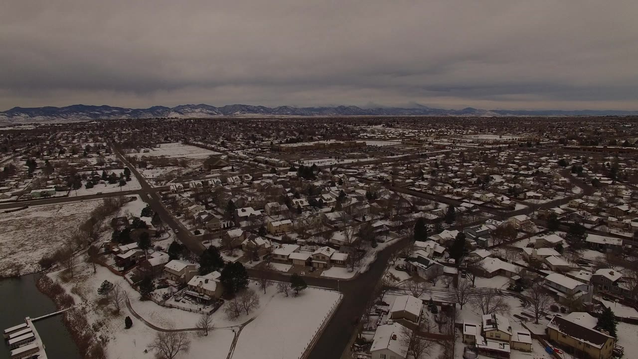 Snowy lakeside neighborhood seen from above under gray clouds.
