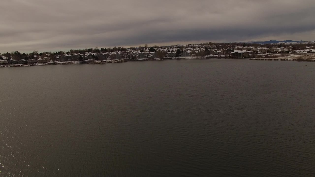 Wide lake water under gray clouds with a distant residential shoreline.