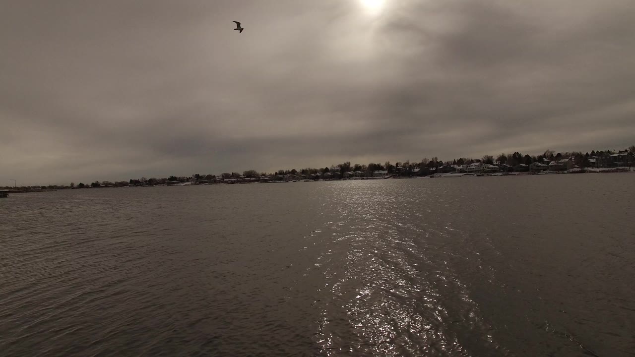 A second wide frame over Jefferson, Colorado water shows the sun glow centered on the ripples, a dark horizontal shoreline, distant houses, and no visible people.