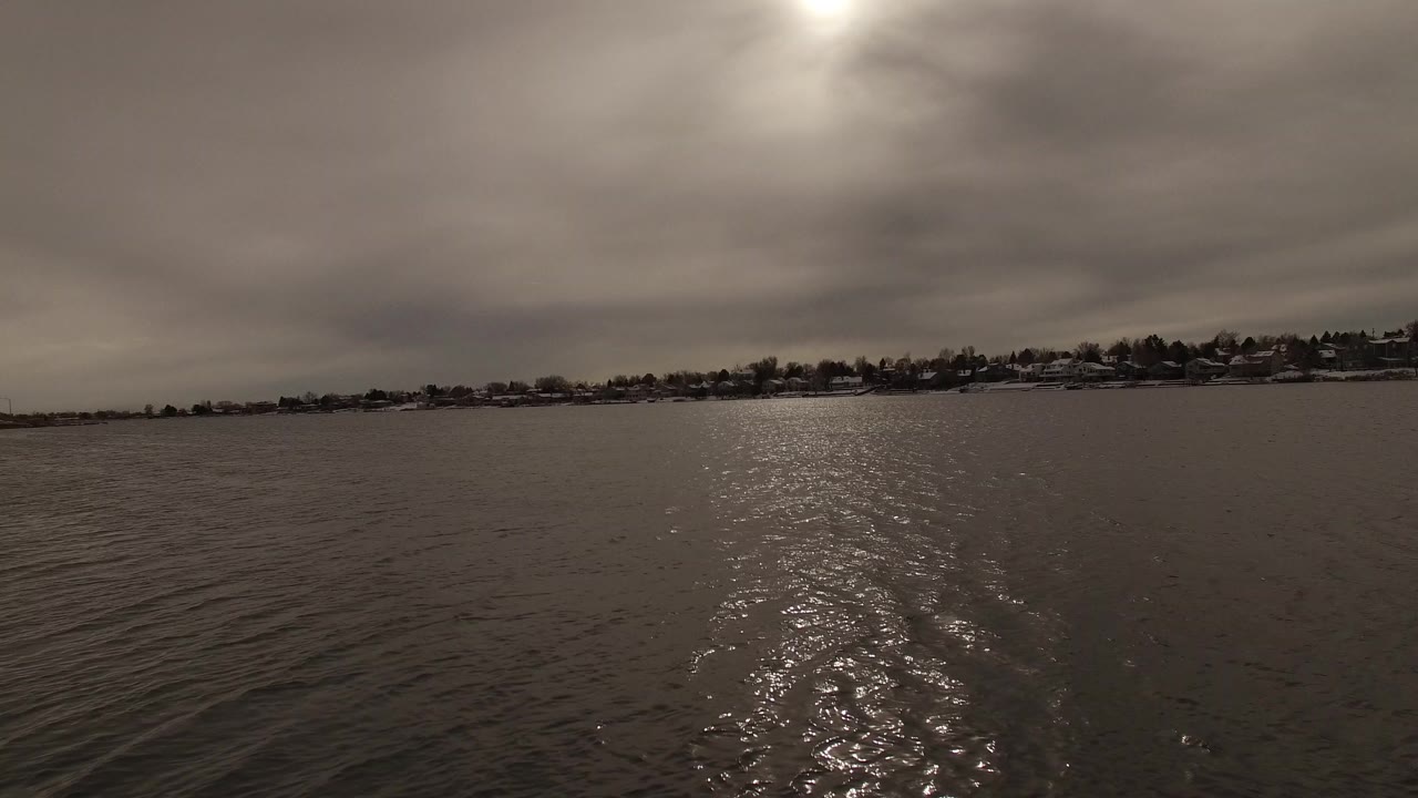 Opening view of rippled water in Jefferson, Colorado, with a dim sun reflection, distant houses along the shoreline, and no visible people.