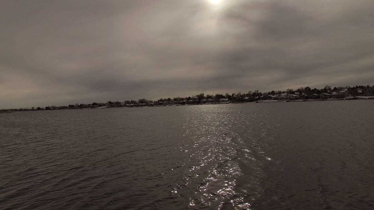 Wide view across rippling water in Jefferson County, Colorado, with a bright reflection on the lake, a low snow-dusted shoreline, and no visible people.