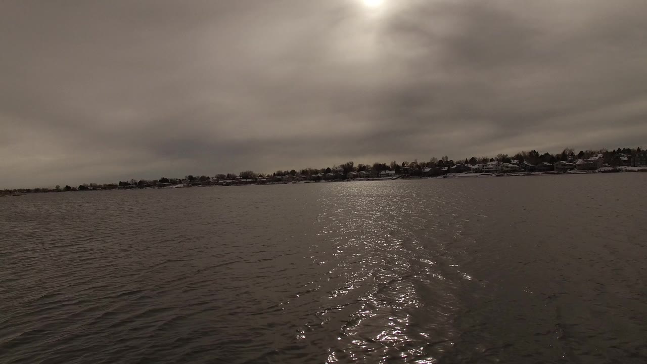 A bright band of reflected light stretches across wavy lake water toward a snowy tree-lined shore in Jefferson County, Colorado, with no visible people.