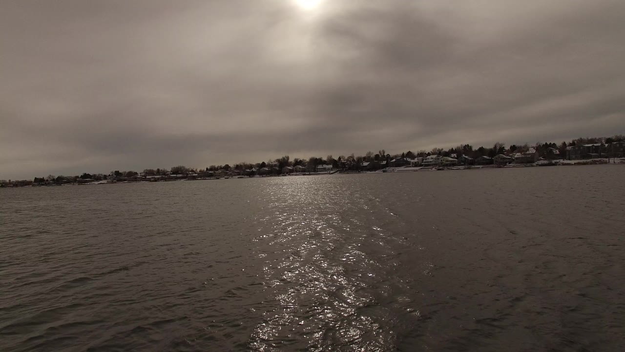 Cloudy aerial view over rippled water with distant shoreline houses.