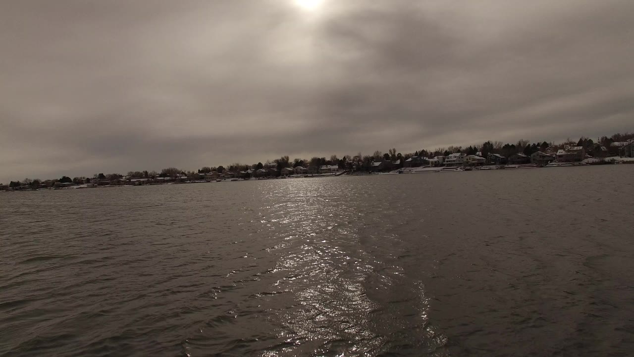Rippling water with distant shoreline homes under a cloudy sky.