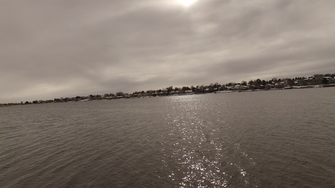 Dark rippled water below a cloudy sky with houses along the far bank.