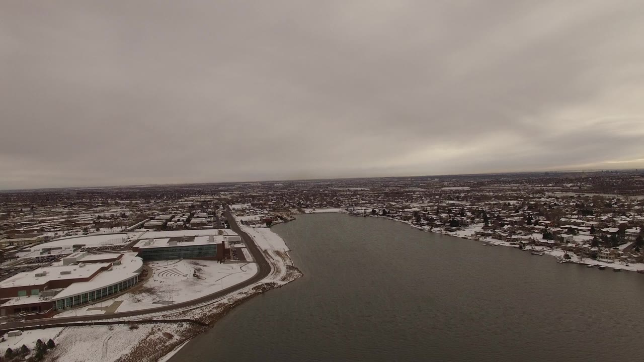 Aerial view over a broad waterway with snowy buildings and roads