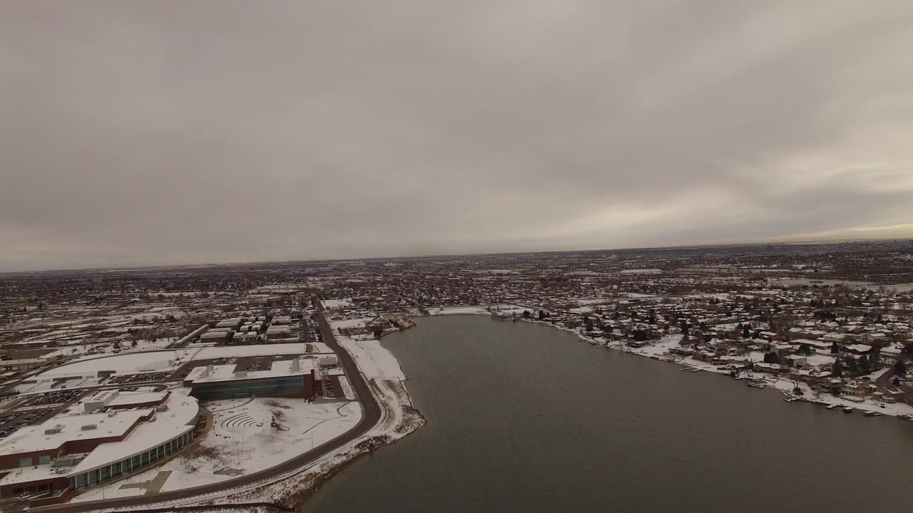 Wide winter view of water, snowy buildings, roads, and a cloudy horizon.