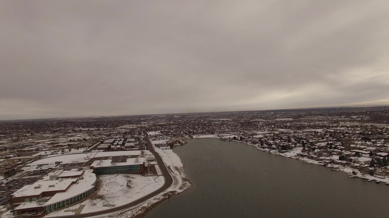 Aerial view of a snow-covered lakeside neighborhood under gray clouds.