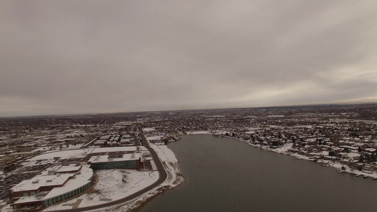 Aerial view in Jefferson County, Colorado with the lake filling the right side, snow-covered buildings and streets on the left, and no visible people.