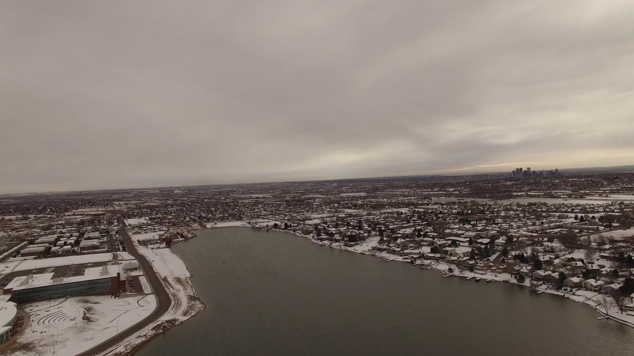 Wide aerial view over a snowy lakefront neighborhood under gray clouds.