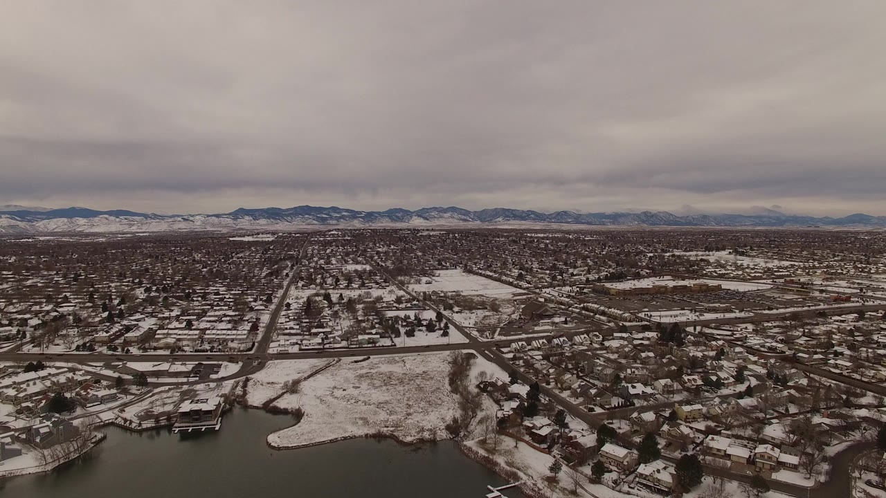 Snowy suburban neighborhood aerial with pond, roads, and distant mountains