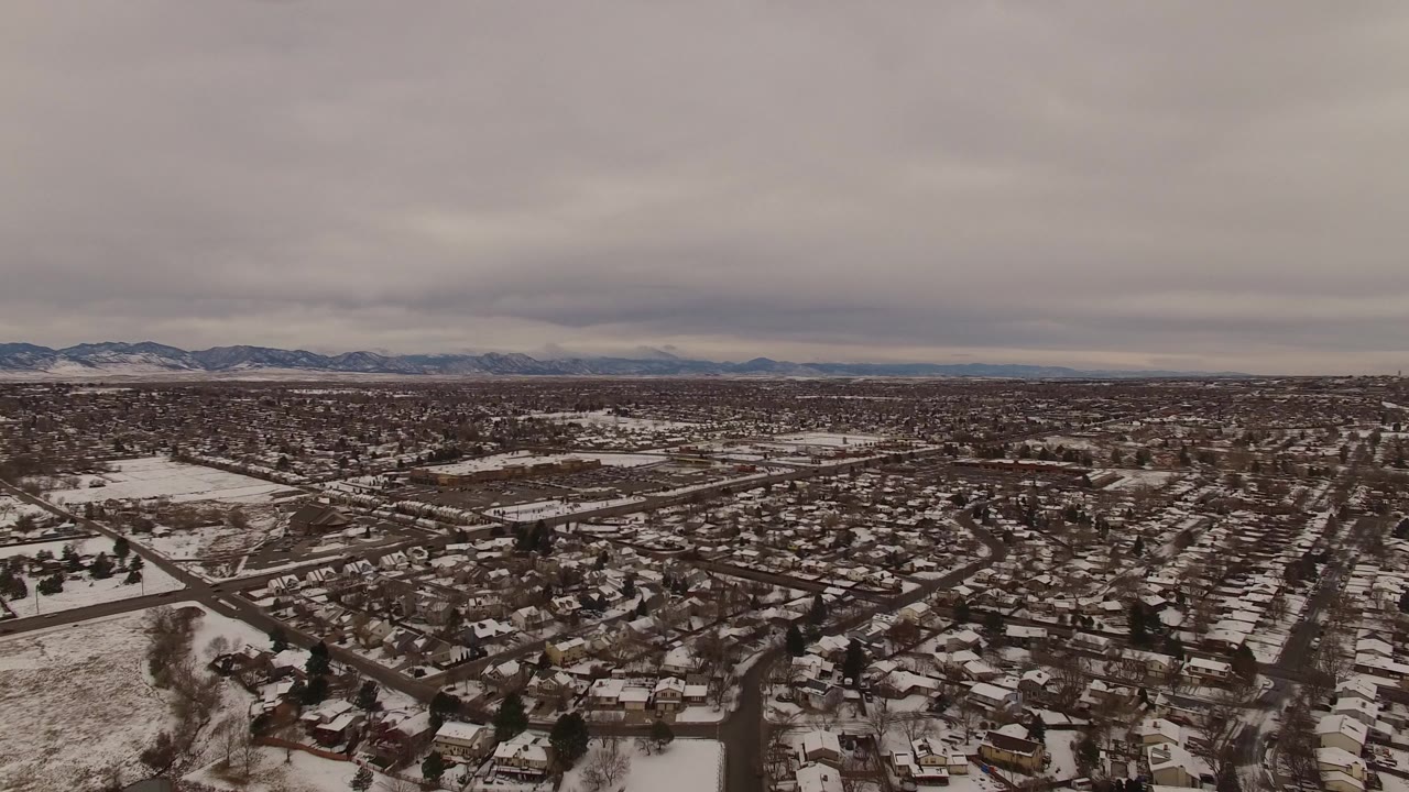 Wide aerial view of snowy residential streets under a gray sky.