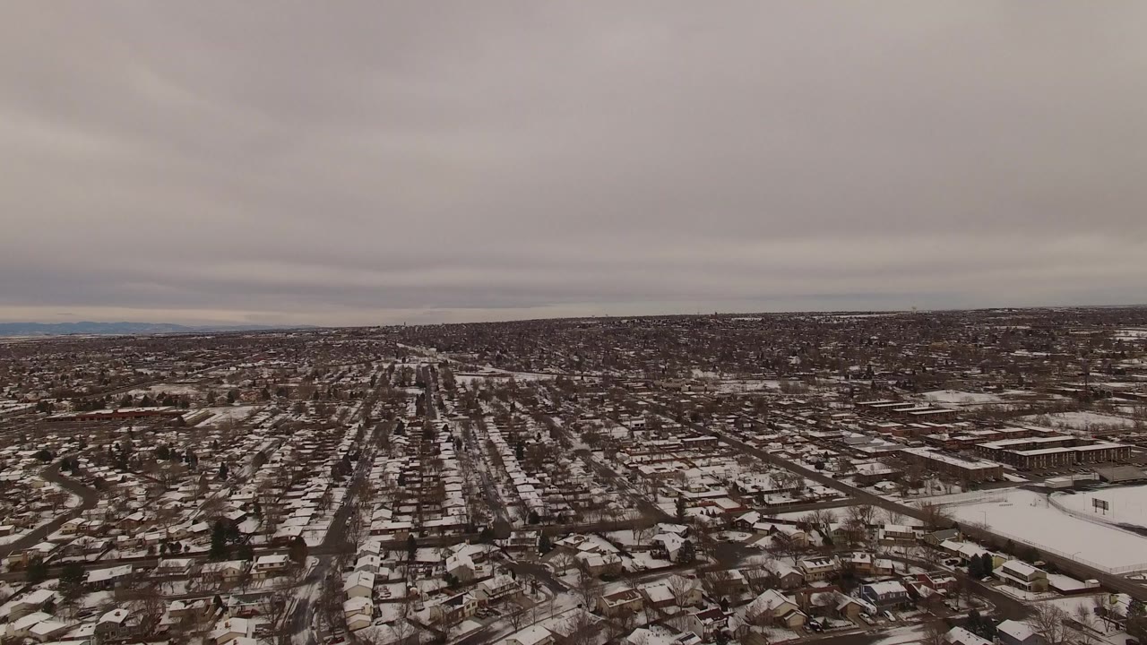 Aerial view across Jefferson County, Colorado, showing rows of houses, pale snow on rooftops and yards, distant terrain, and no visible people.