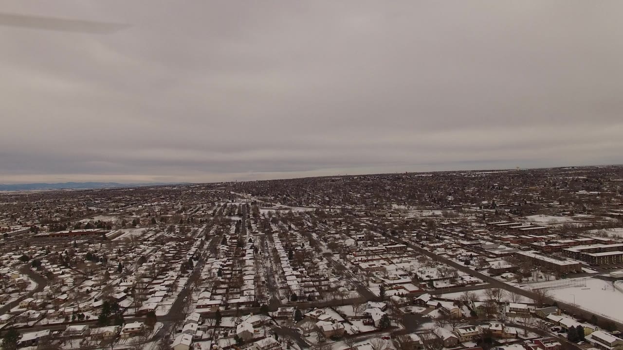 Aerial view over snowy suburban streets under gray clouds