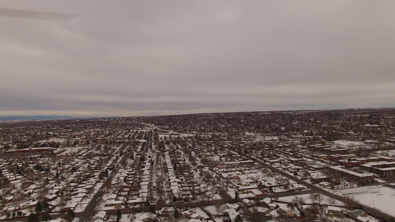 A high view across Jefferson County, Colorado showing rows of homes, road grids, snow-covered fields, muted winter light, and no visible people.