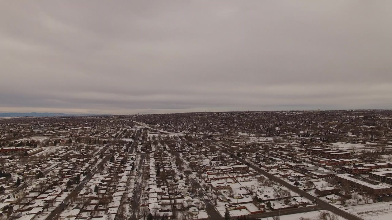 Wide aerial view of snowy suburban streets under gray clouds