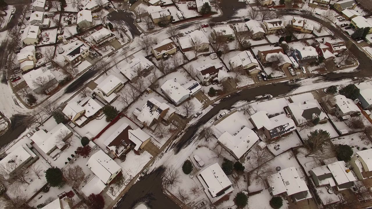 Overhead aerial view of snow-covered homes and curved residential streets in Jefferson County, Colorado, with bare trees and no visible people.