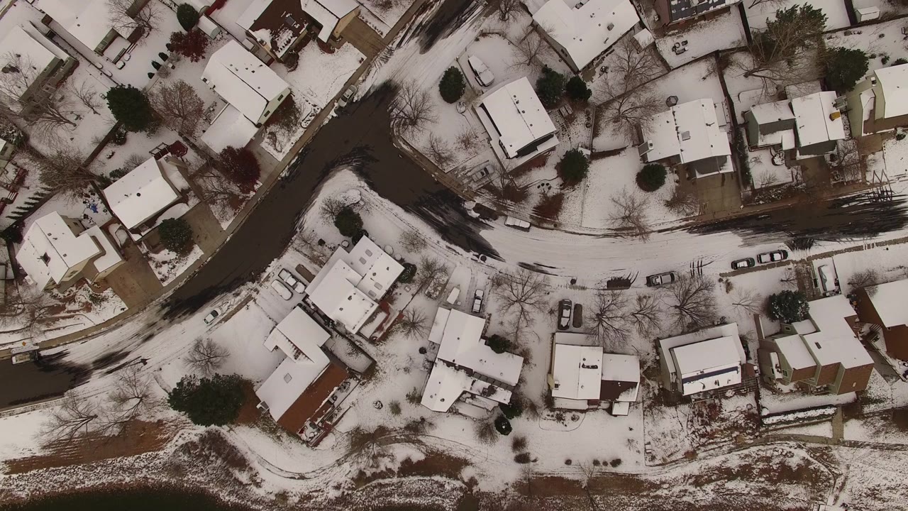 Vertical aerial frame in Jefferson County, Colorado showing clustered houses, white roofs, dark asphalt streets, leafless trees, parked vehicles, and no visible people.