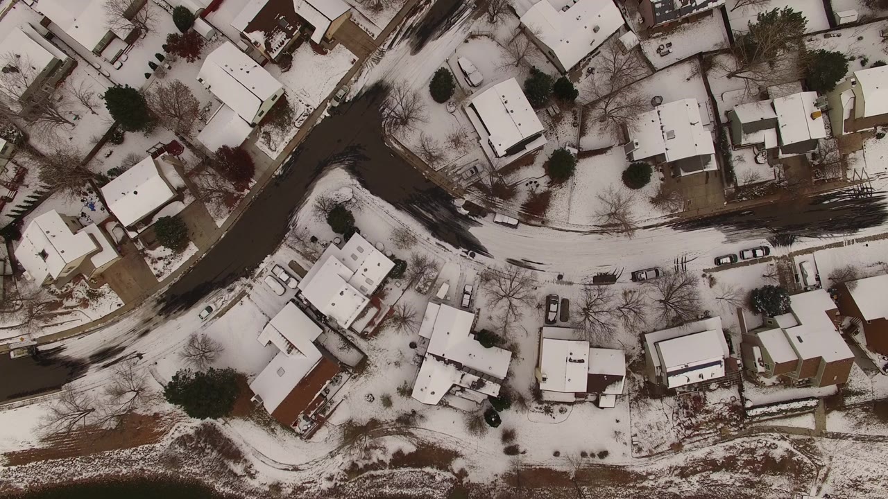 Aerial winter suburb with houses, cars, and bare trees.