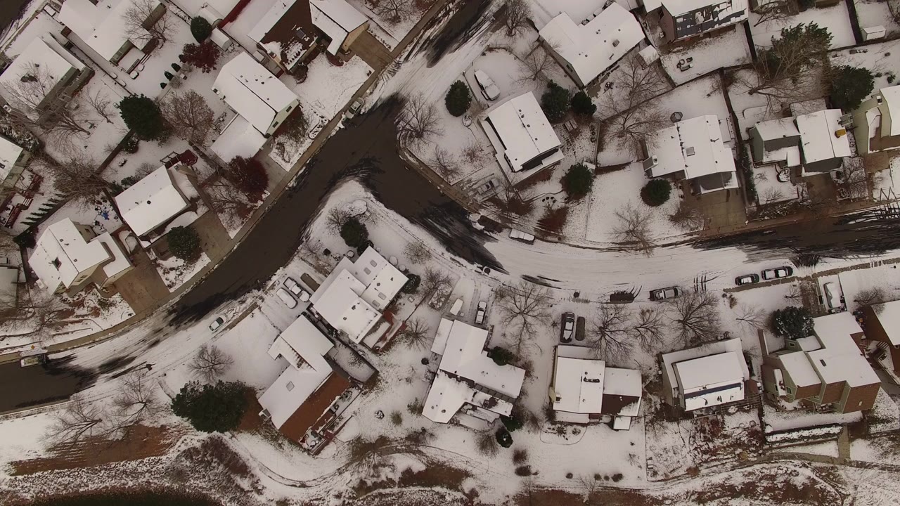 Top-down aerial view of snow-covered homes, bare trees, parked cars, and curving roads in Jefferson County, Colorado, with no visible people.