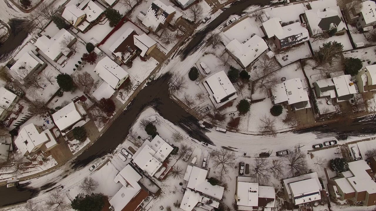 High overhead view of snow-covered residential blocks in Jefferson County, Colorado, with dark roads, bare trees, parked cars, and no visible people.