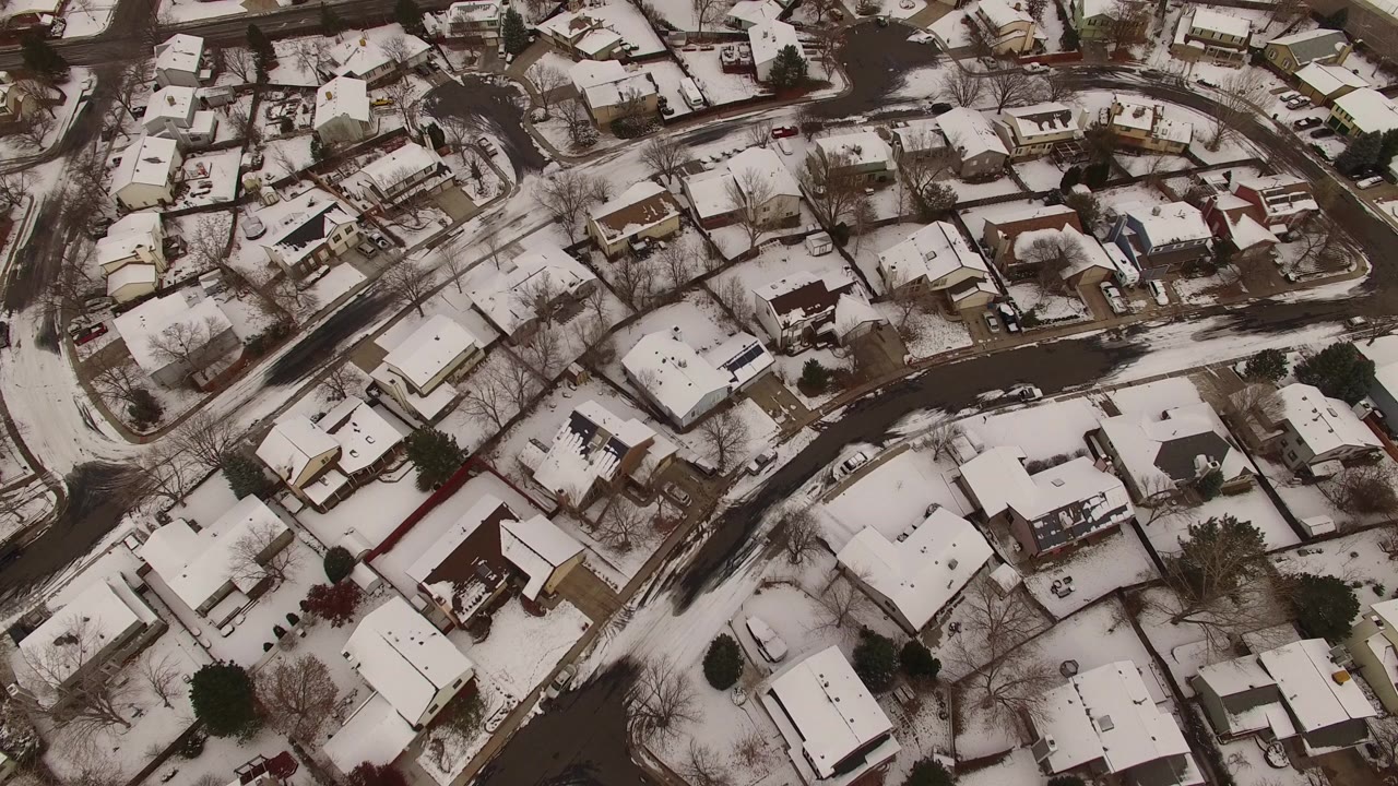 Aerial view over Jefferson County, Colorado homes with snow on roofs and yards, bare trees along curved streets, and no visible people at the start of the clip.